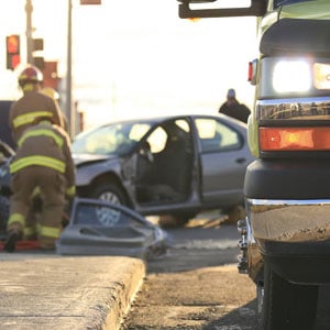 A rescue worker stands next to a wrecked car at the scene of a car accident.