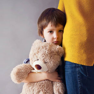 Child standing with teddy bear near woman