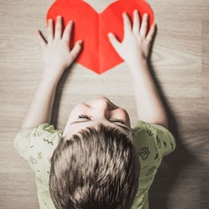 A child holds a red heart-shaped paper, symbolizing a custody battle, with emotions and love at stake.