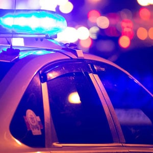 A police car with blue lights flashing at night, indicating an emergency response.