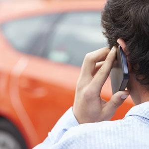 A man using his phone in front of a car after an accident.